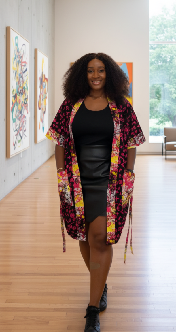 Woman in a colorful ankara kimono standing in an art gallery with paintings on the wall.
