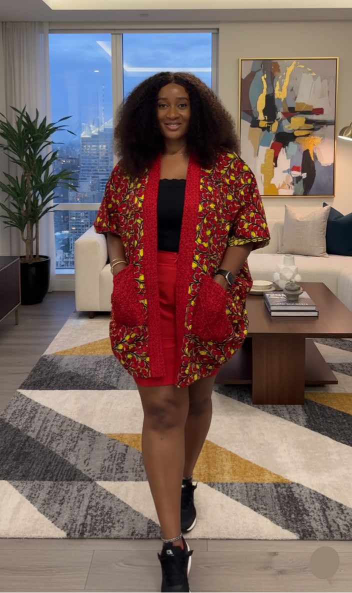 Woman in a red ankara outfit standing in a modern living room with large windows and decorative elements.
