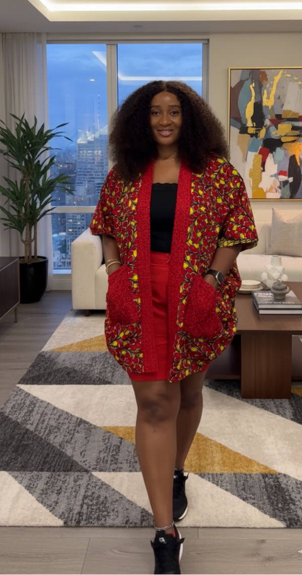 Woman in a red ankara kimono outfit standing in a modern living room with large windows and decorative elements.